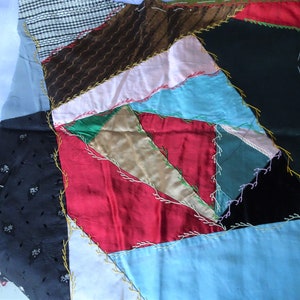 May include: A patchwork quilt featuring a variety of colours and patterns, including red, blue, black, green, and brown. The quilt is made from different fabrics and is stitched together with a decorative stitch.