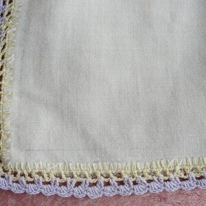 May include: A white linen handkerchief with a crocheted border in shades of purple and yellow.