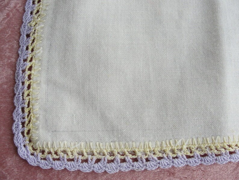 May include: A white linen handkerchief with a crocheted border in shades of purple and yellow.