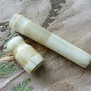 May include: Two ivory-colored, cylindrical containers with a ribbed texture. The containers are made of bone or ivory and have a smooth, polished finish.