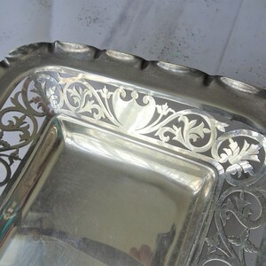 K&ouml;nnte beinhalten: Ein rechteckiges Serviertablett aus Silber mit gewelltem Rand und aufwendigen durchbrochenen floralen und scrollartigen Designs. Das Tablett hat eine hochglanzpolierte, reflektierende Oberfl&auml;che, und der dekorative Rand verleiht dem St&uuml;ck eine elegante Note.