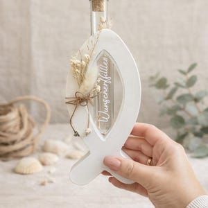 Peut inclure: Objet décoratif blanc en forme de poisson avec une fiole en verre et un bouchon en liège. La fiole contient des fleurs séchées et le texte "Wunscherfüller" est visible. Un nœud en ficelle et des ornements ajoutent des détails.