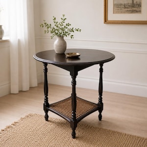 Peut inclure: Une table d'appoint ronde en bois brun foncé dotée de quatre pieds tournés et d'une étagère carrée inférieure avec un insert en cannage tressé. Un vase en céramique clair contenant des tiges feuillues vertes et une petite coupelle en laiton.