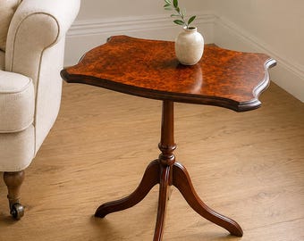 Peut inclure: Une table d'appoint à piédestal en bois avec un plateau rectangulaire en placage de ronce de noyer brun foncé et des bords festonnés. La table repose sur une colonne centrale tournée soutenue par trois pieds incurvés. Un petit vase en céramique crème est posé dessus.