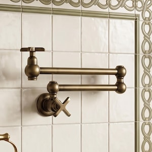 May include: A wall-mounted pot filler faucet with a double-jointed swing arm and a cross-handle design. The fixture features a brushed antique brass finish, two articulated horizontal arms, and a single control valve at the base for water flow.