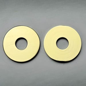 May include: Two gold-colored, circular objects with a hole in the center. The objects have a smooth, reflective surface and a dark edge. They are set against a gray background.