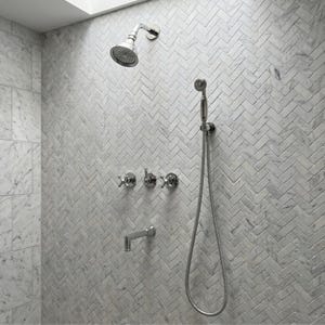 May include: A contemporary shower featuring a silver shower head, a handheld shower, and faucet fixtures. The shower wall is tiled with white and grey herringbone tiles. The fixtures are silver.