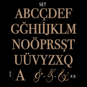 以下が含まれることがあります： 黒い背景にベージュのセリフ体大文字と記号のセット。文字にはA、B、C、&Ccedil;、D、E、F、G、Ğ、H、I、J、K、L、M、N、O、&Ouml;、P、R、S、Ş、T、U、&Uuml;、V、Y、Z、X、Q、およびアンパサンドが含まれます。6cmのスケールマーカーが表示されています。