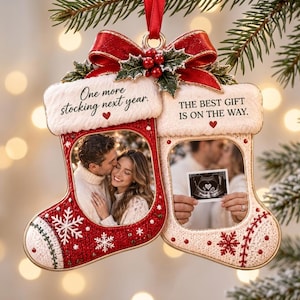 Op de afbeelding: Een dubbele kerstsok-ornament met een rood-witte gebreide textuur, een rode strik en hulst bovenaan. De linker sok toont een foto van een koppel, de rechter een echo. Tekst: One more stocking next year. THE BEST GIFT IS ON THE WAY.