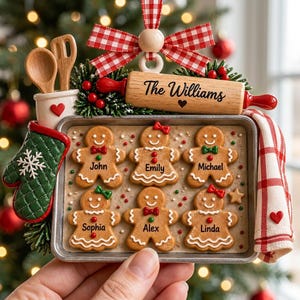 Könnte beinhalten: Ein Weihnachtsschmuck mit einem Backblech und sechs Lebkuchenmännern mit den Namen John, Emily, Michael, Sophia, Alex und Linda. Dazu gehören ein Nudelholz mit der Aufschrift The Williams, ein grüner Ofenhandschuh, ein Holzlöffel und eine rote Schleife.