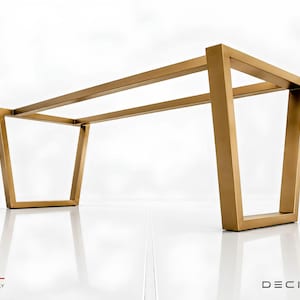 Può includere: Una base per tavolo in metallo dorato con una cornice rettangolare e quattro gambe inclinate che si allargano verso l'esterno. La struttura è composta da barre metalliche piatte e lineari collegate per formare un supporto aperto e robusto.