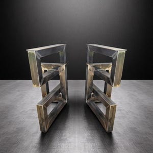 Könnte beinhalten: Zwei Metall-Tischbeine mit geometrischem Design. Die Beine bestehen aus geschweißtem Stahl und haben ein rohes, industrielles Finish. Das Design weist abgewinkelte Stützen und eine flache Oberseite auf. Geeignet für einen Tisch im modernen oder industriellen Stil. Höhe ca. 76 cm.
