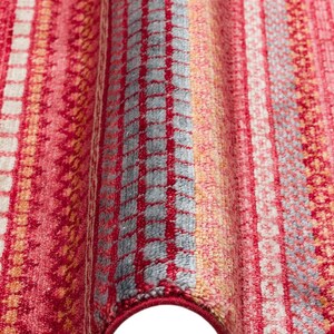 May include: A textile rug featuring a vibrant pattern of vertical stripes in shades of red, pink, orange, and light blue. The surface displays a variety of woven textures, including grid-like squares, horizontal bands, and intricate geometric motifs.
