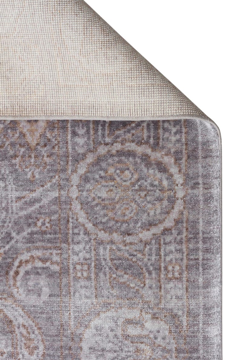 May include: A rectangular area rug featuring a muted gray and beige color palette with a repeating medallion and floral pattern. The corner of the rug is folded over to reveal a light beige, textured woven backing and a finished bound edge.