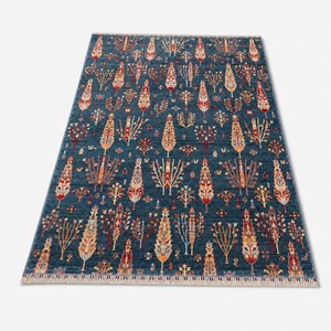 May include: A rectangular area rug featuring a deep blue background with a repeating pattern of stylized trees and floral motifs in shades of red, orange, cream, and light blue. The rug has a short fringe along the top and bottom edges.