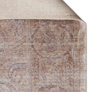 May include: A rectangular area rug featuring a faded, distressed pattern in shades of taupe, beige, and soft blue. The rug has a visible woven backing in a light cream color, with one corner folded over to reveal the textured underside and edge.
