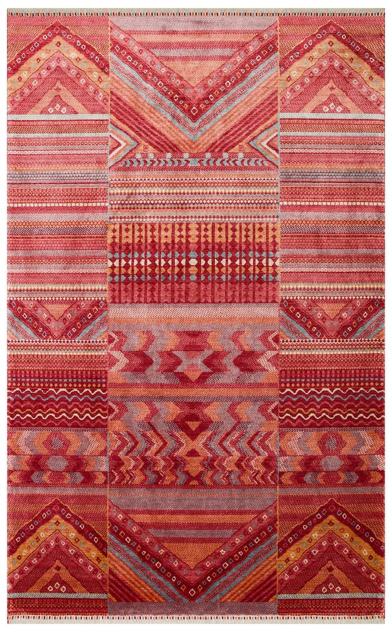 May include: A rectangular area rug featuring a vibrant palette of red, orange, and pink tones. The design consists of repeating horizontal bands with intricate geometric patterns, including chevrons, zigzags, and small squares, with fringe.