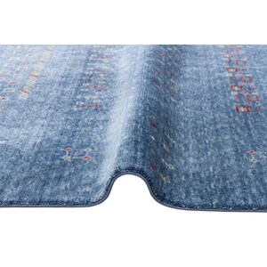 May include: A blue area rug with a textured, soft pile surface featuring a repeating pattern of small, scattered geometric shapes in red, white, and yellow. The rug is folded over to reveal its thickness and the finished, bound edge along the bottom.