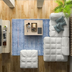 May include: A white tufted sectional sofa with a matching ottoman, positioned on a blue patterned area rug. A light wood coffee table sits in the center, holding a tray with small decorative items, a book, and a black rectangular object.