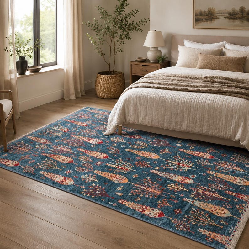 May include: A rectangular area rug featuring a deep blue background with a repeating pattern of stylized trees and floral motifs in shades of orange, red, cream, and brown. The rug has a short fringe along the edges and a flat-woven texture.