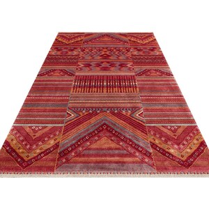 May include: A rectangular area rug featuring a vibrant red, orange, and maroon color palette with intricate geometric patterns, horizontal stripes, and chevron motifs. The rug has a short fringe along the bottom edge and a symmetrical design.