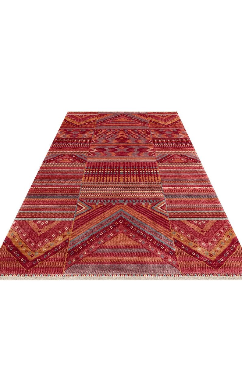 May include: A rectangular area rug featuring a vibrant red, orange, and maroon color palette with intricate geometric patterns, horizontal stripes, and chevron motifs. The rug has a short fringe along the bottom edge and a symmetrical design.