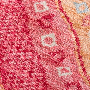 May include: A tufted textile featuring a dense, looped pile surface with a vibrant color palette of deep magenta, bright pink, soft peach, and orange. The design includes repeating geometric floral motifs in white and light blue accents.