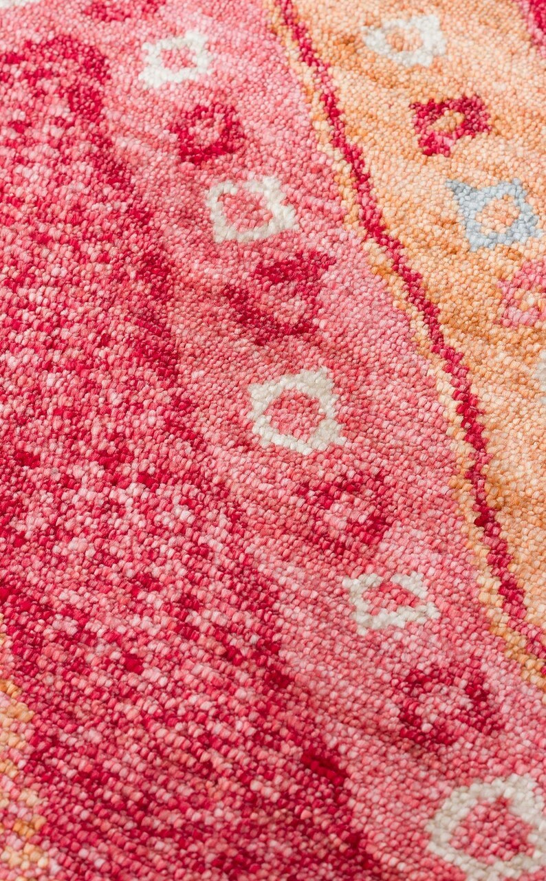 May include: A tufted textile featuring a dense, looped pile surface with a vibrant color palette of deep magenta, bright pink, soft peach, and orange. The design includes repeating geometric floral motifs in white and light blue accents.