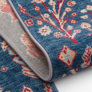 May include: A blue area rug featuring a repeating floral pattern in shades of red, cream, and light blue. The rug has a thick, textured pile and is finished with a grey serged edge that highlights the construction of the fabric and the backing.