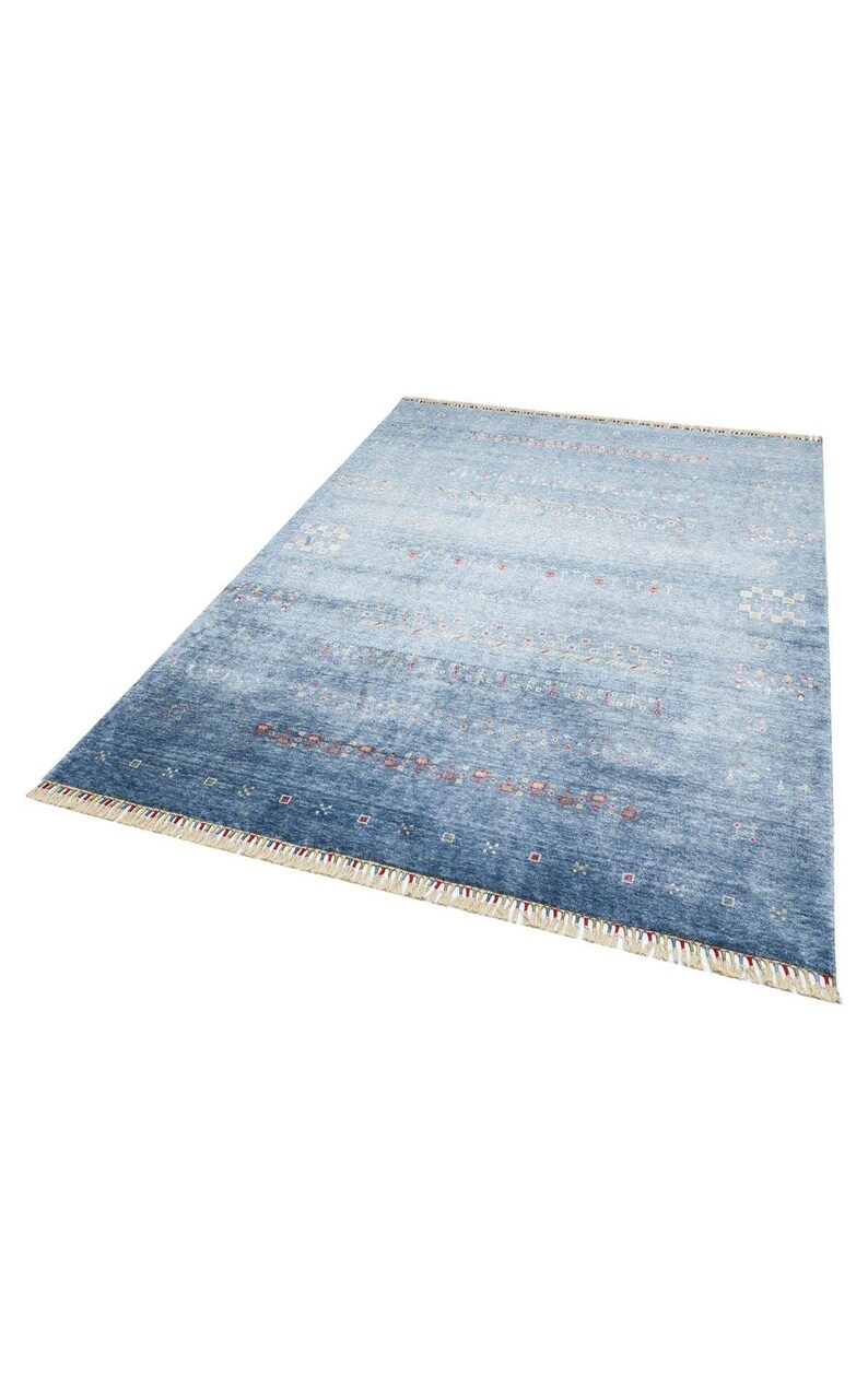 May include: A rectangular area rug featuring a gradient of blue tones, ranging from light to deep navy. The surface is decorated with horizontal rows of small, intricate geometric patterns in white and red, finished with cream-colored fringe.