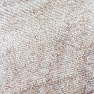 May include: A close-up view of a woven rug featuring a soft, neutral color palette. The surface displays a dense, textured pile with a subtle, faded pattern in shades of cream, beige, and light taupe, creating a soft and uniform appearance.