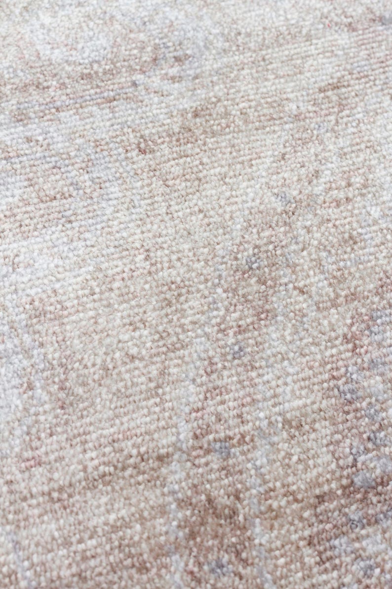 May include: A close-up view of a woven rug featuring a soft, neutral color palette. The surface displays a dense, textured pile with a subtle, faded pattern in shades of cream, beige, and light taupe, creating a soft and uniform appearance.