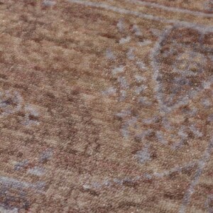 May include: A textured area rug featuring a faded, distressed pattern in shades of warm brown, tan, and muted grey. The surface displays a dense, low-pile weave with intricate, weathered floral and geometric motifs distributed across the fabric.