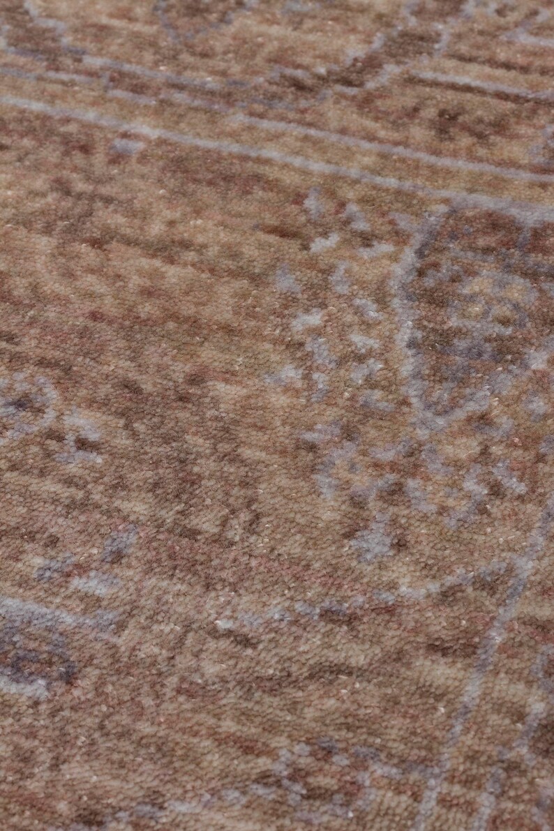 May include: A textured area rug featuring a faded, distressed pattern in shades of warm brown, tan, and muted grey. The surface displays a dense, low-pile weave with intricate, weathered floral and geometric motifs distributed across the fabric.