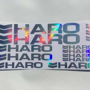 May include: A white sticker with the word "HARO" repeated multiple times in a black, iridescent font. The sticker also features a repeating pattern of black arrows.