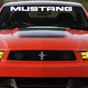 Könnte beinhalten: Vorderansicht eines roten Mustang-Autos mit dem Wort "MUSTANG" in Weiß oben auf der Windschutzscheibe. Das Auto hat schwarze Akzente, einen schwarzen Motorhaubenstreifen und ein Chromemblem.