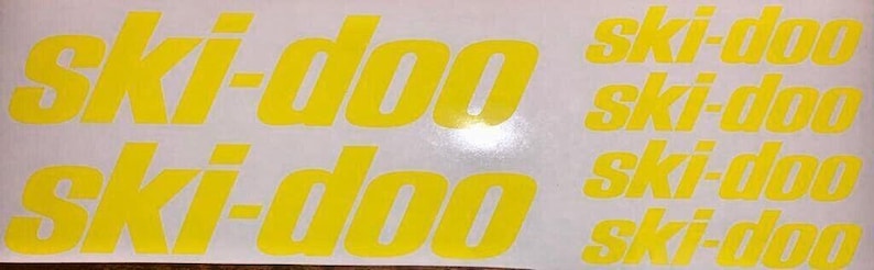 Puede incluir: Cuatro calcoman&iacute;as de vinilo amarillo con el texto "ski-doo" impreso en ellas. Las calcoman&iacute;as est&aacute;n sobre un fondo blanco.