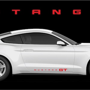 May include: A white Mustang GT sports car is shown in profile against a black background. The word "MUSTANG" is above the car in red block letters, with "GT" to the right. The car has red "MUSTANG GT" lettering on the side.