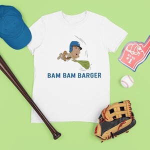 May include: White t-shirt with a baseball-themed graphic and the text "BAM BAM BARGER". Includes a blue baseball cap, a brown baseball bat, a baseball glove, a foam finger, and a baseball.