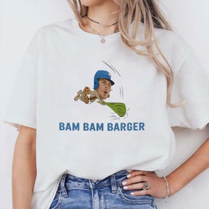 May include: White t-shirt with a cartoon baseball player illustration and the blue text "BAM BAM BARGER". The graphic shows a player wearing a blue helmet and uniform.