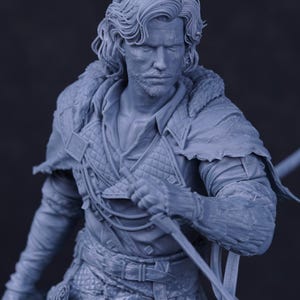 May include: A detailed, monochromatic figurine of a man in medieval attire. The figure has long, wavy hair and a beard. He wears a textured tunic, a fur-lined cloak, and holds a sword. The overall aesthetic suggests a fantasy or historical theme.