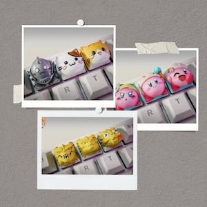 May include: A collection of custom keycaps featuring various cartoon characters. The keycaps are in the shape of a cat, a robot, and characters from the Kirby video game series. The keycaps are in various colors, including white, orange, yellow, and pink.