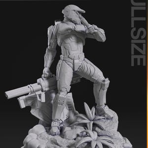 May include: A gray, full-size figurine of a futuristic soldier holding a rifle, standing on a rocky base with foliage. The figurine is detailed with armor and a helmet. The words "nomnom Figures TURNTABLE" are in the top left.