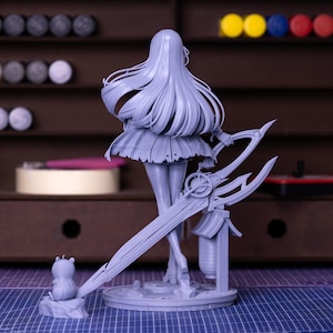 Puede incluir: Una figura gris sin pintar de un personaje femenino con cabello largo y suelto, sosteniendo un arma grande y ornamentada. La figura est&aacute; sobre una base circular, con una peque&ntilde;a figura de animal cerca. El fondo incluye una estanter&iacute;a de madera con materiales de pintura.