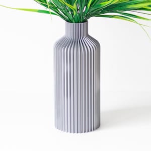 Pode incluir: Um vaso de cerâmica cinza com um design canelado. O vaso está vazio e tem uma forma alta e fina.