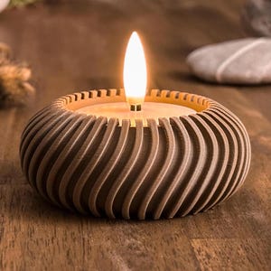 Può includere: Un portacandele marrone con un designo a spirale e texture. Il portacandele ha una piccola candela bianca all'interno che è accesa.