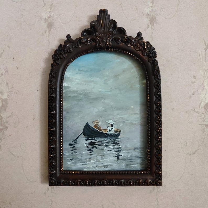 Puede incluir: Una pintura enmarcada de dos personas en un bote de remos en un cuerpo de agua tranquilo. El cielo es de un azul claro con nubes blancas. El bote es de color marr&oacute;n oscuro y las personas llevan sombreros blancos.