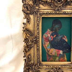 May include: A framed oil painting featuring a person with dark skin wearing a multicolored patterned shirt, holding a black swan against a deep teal background. The artwork is encased in an ornate, antique-style gold frame with intricate carvings.