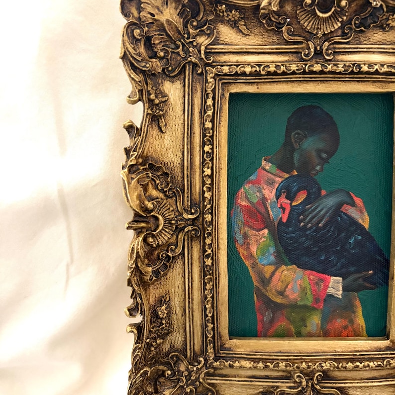 May include: A framed oil painting featuring a person with dark skin wearing a multicolored patterned shirt, holding a black swan against a deep teal background. The artwork is encased in an ornate, antique-style gold frame with intricate carvings.