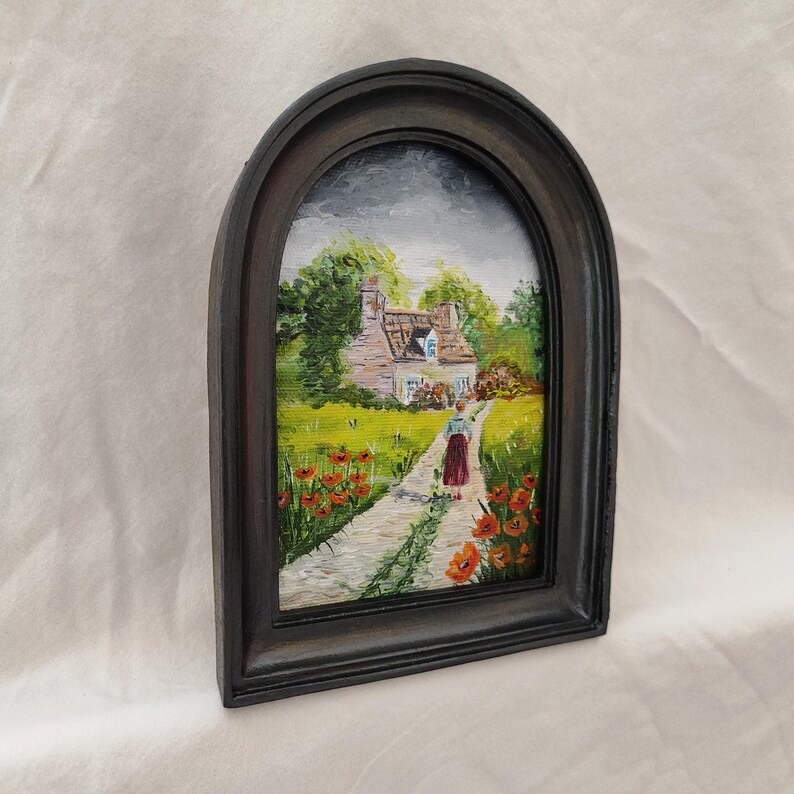 May include: Oil painting in a dark gray arched frame. The artwork depicts a cottage scene with a path leading to a house. A person in a red skirt walks along the path, surrounded by green grass and red flowers. The sky is overcast.